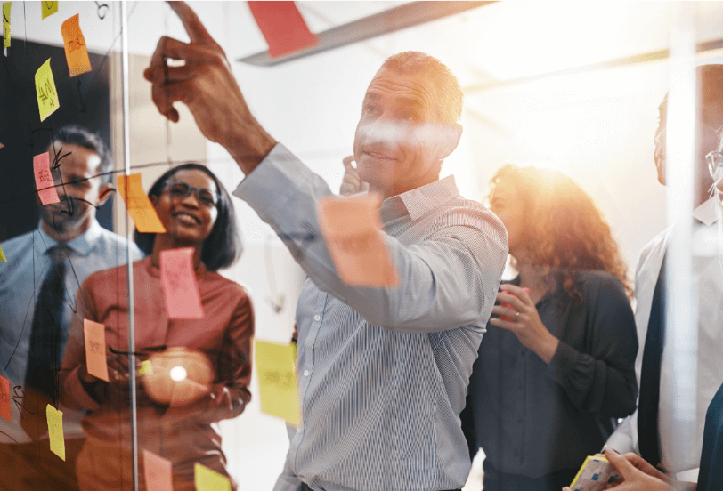 A group of people discussing points from sticky notes on glass wall