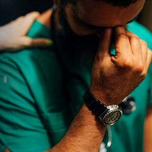 A male nurse having holding his hand to his head